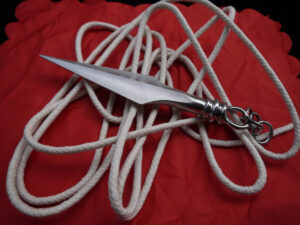 Modern rope dart weapon featuring a sharp metal dart attached to a long white rope, displayed on red fabric. The rope dart, originating from the Tang Dynasty, evolved from a hidden weapon into a martial arts tool and performance instrument.